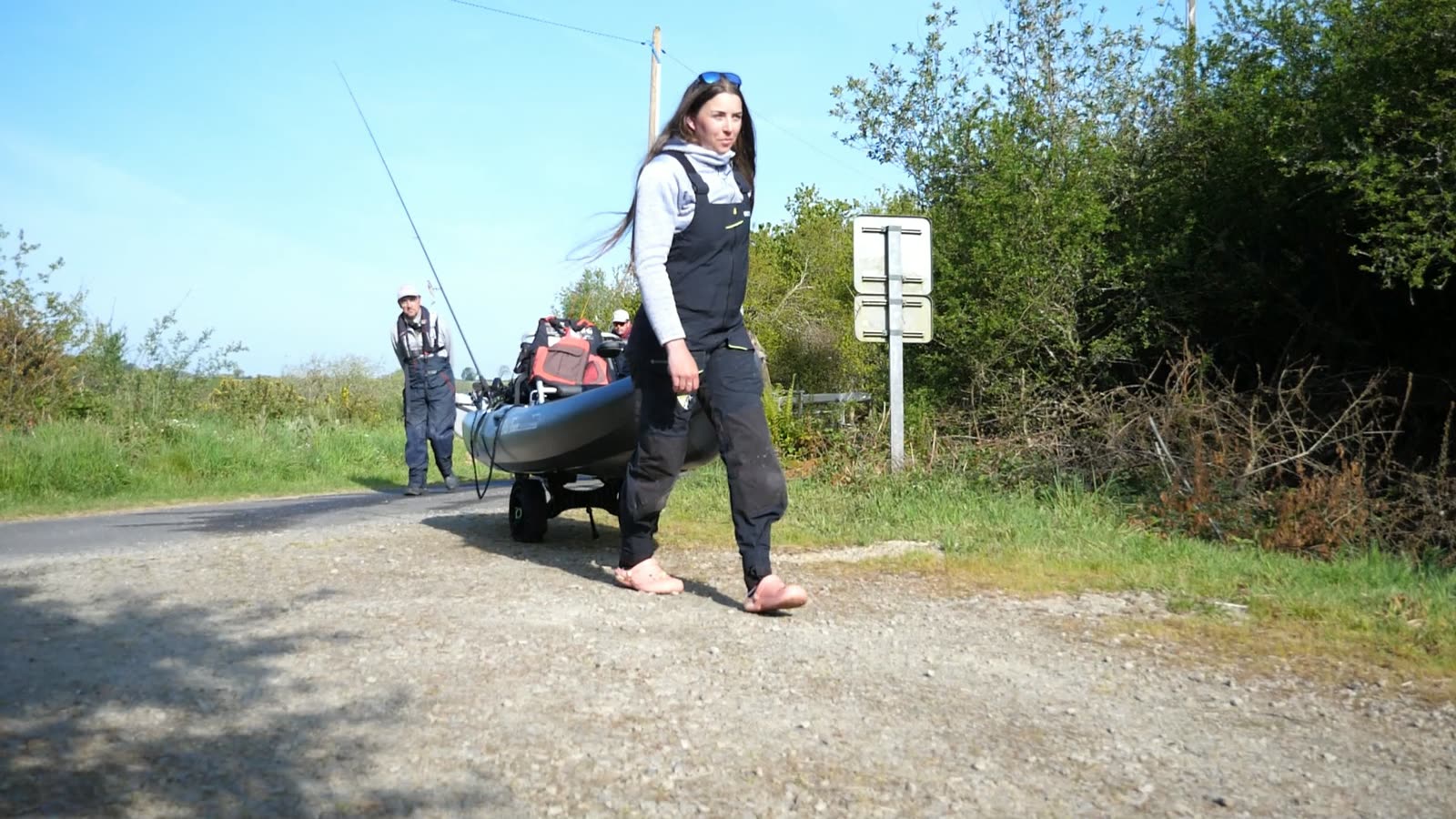 Pêcheuse en waders tirant son kayak de pêche sur un chemin