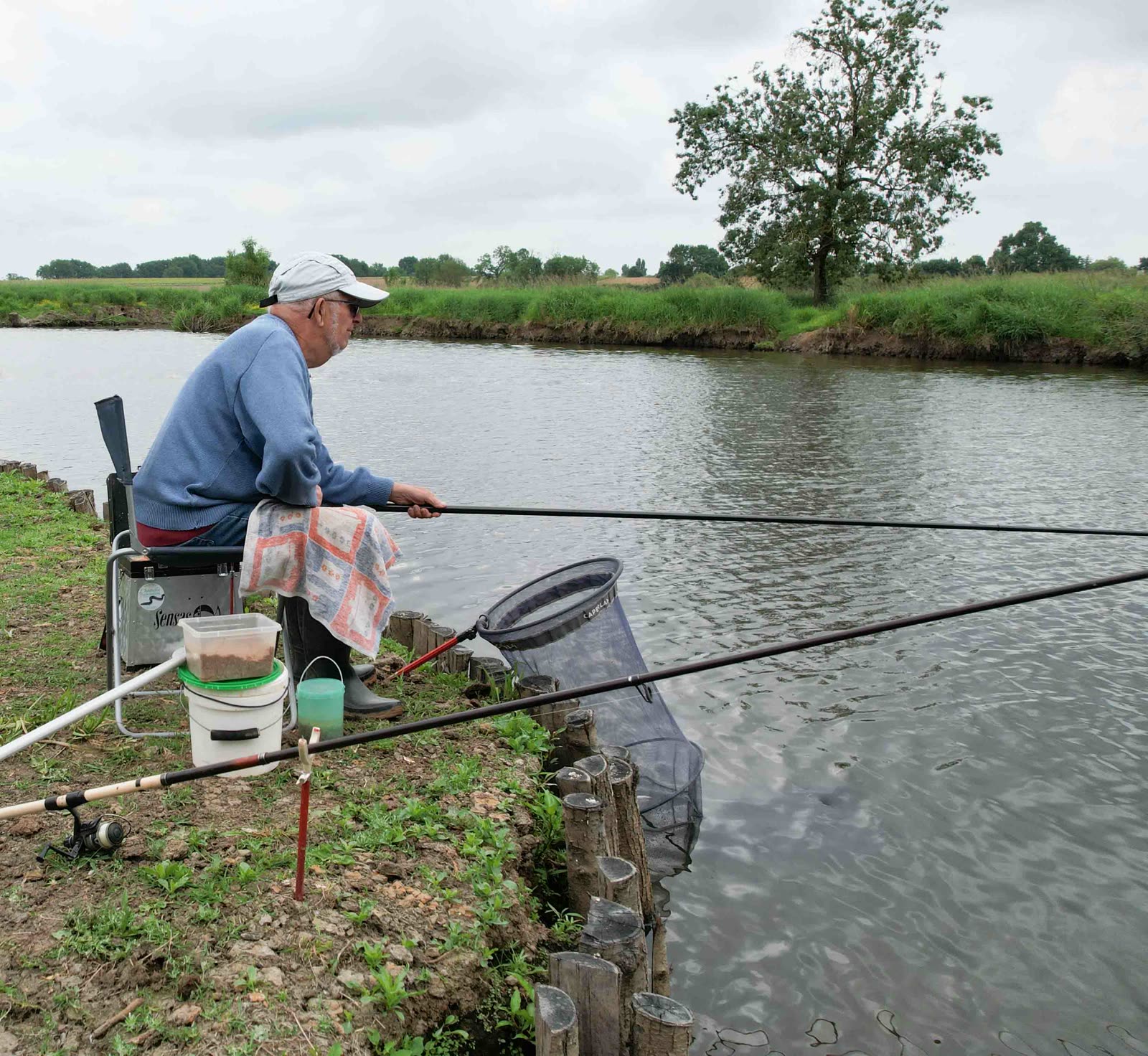Pêcheur au coup assis au bord de la rivière, épuisette et bourriche à l’eau